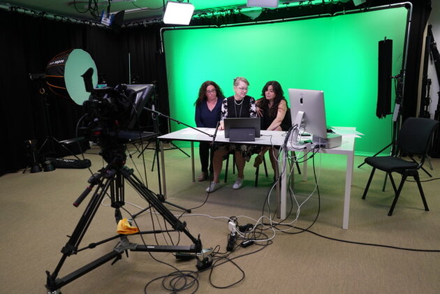 videocamera pointed to three women in front of a green screen